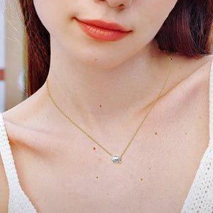 Gold bezel necklace with emerald cut moissanite pendant on a delicate chain