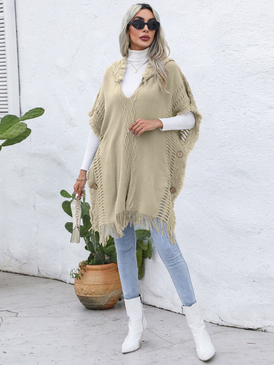 Khaki knit poncho with fringe, wooden buttons, and textured pattern.