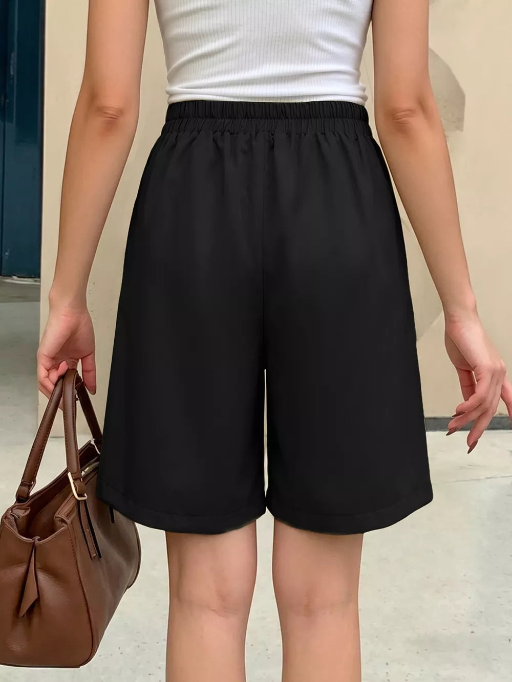 Black chino shorts with high waist and elastic waistband, styled with a white tank top and brown handbag.