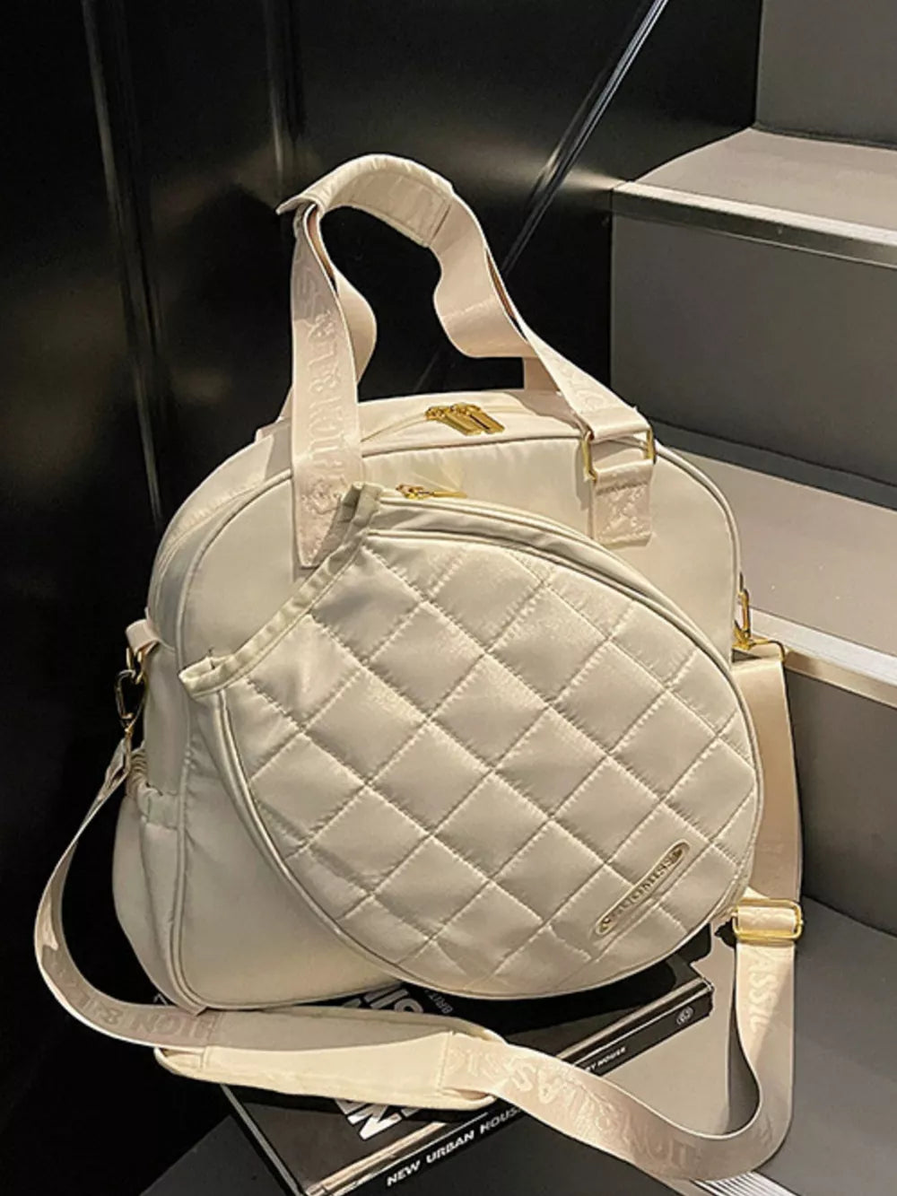 Quilted Oxford bag in off-white with adjustable strap and racket compartment.