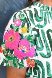 Women's abstract print puff sleeve top with floral embroidery in pink and orange.