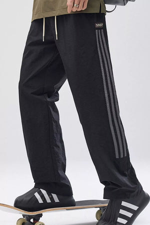Black casual drawstring sweatpants with side stripes and a logo detail.