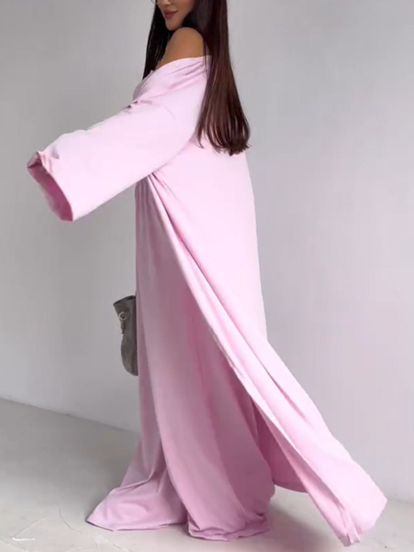 Blush pink off-the-shoulder maxi dress with long sleeves and high slits, styled with a grey bag.