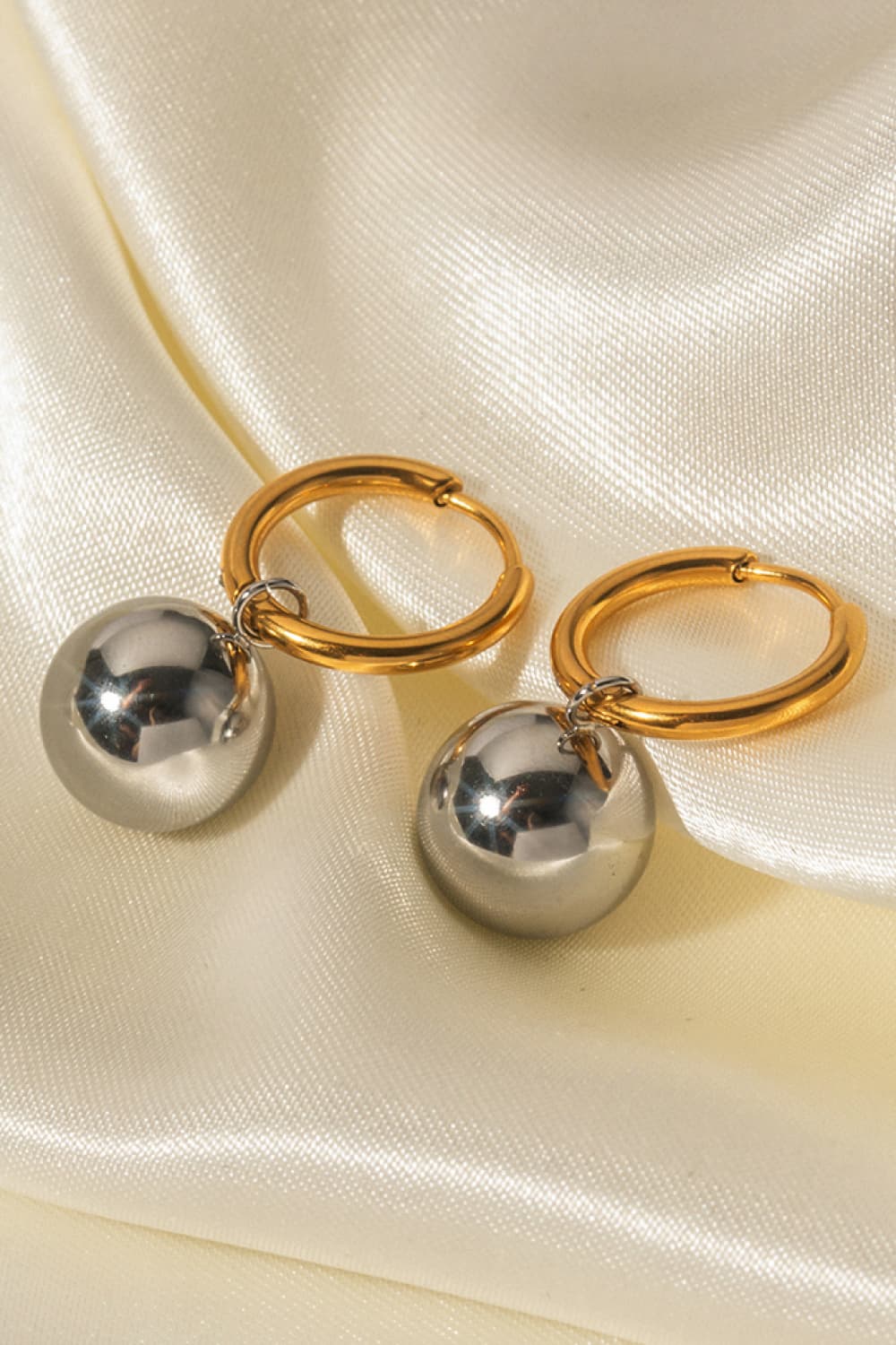 Orbital gold hoop earrings with silver sphere drops.