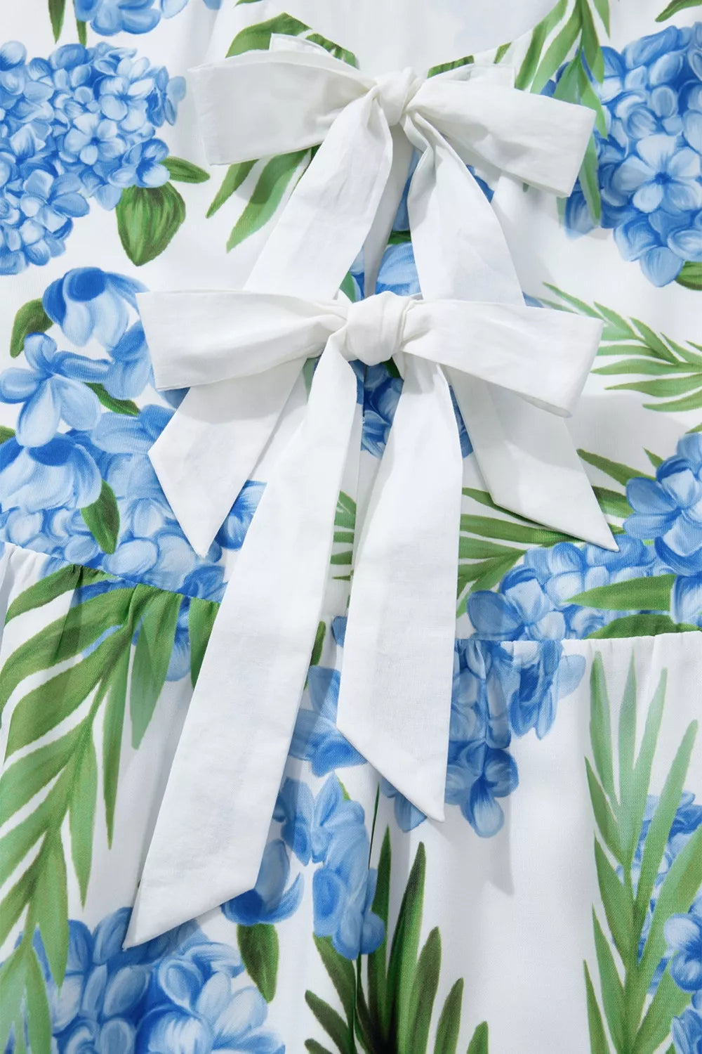 Ruffled mini dress with hydrangea and palm print, featuring white bow details.