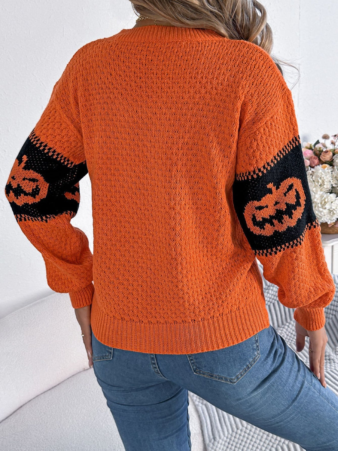 Orange acrylic knit sweater with black intarsia jack-o'-lantern sleeves and a textured knit body.