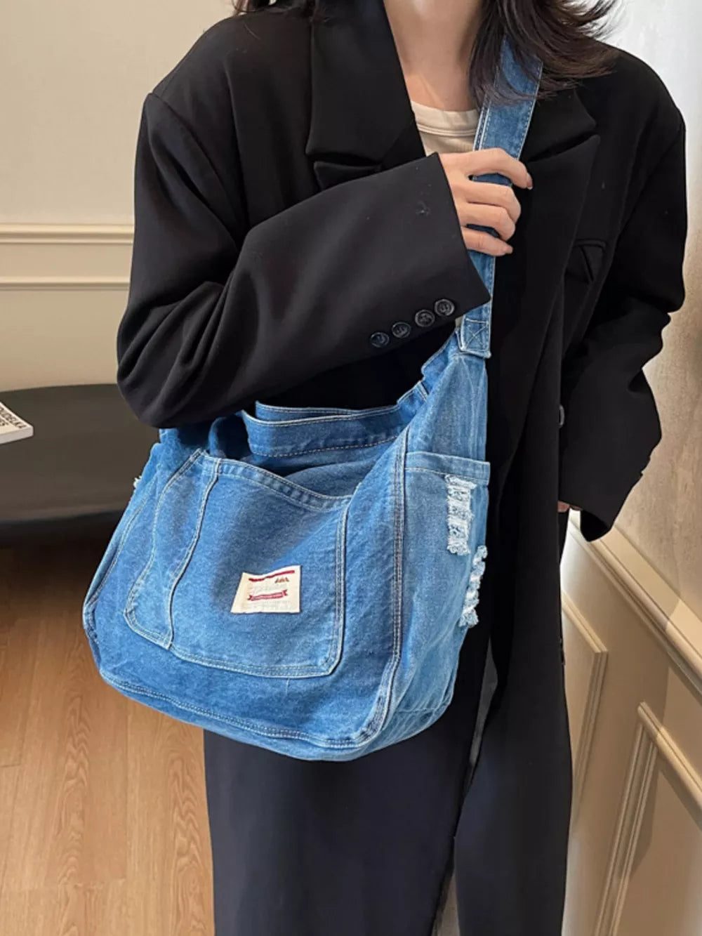 Slouchy blue denim crossbody bag with contrast stitching and distressed details.