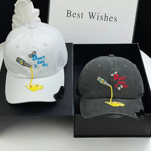 White and dark gray baseball caps with cartoon embroidery of a bottle pouring liquid.