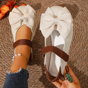 Beige textured round toe flats with large bow detail and brown ankle strap.