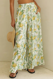 Botanical print palazzo trousers in white with yellow pineapples and green leaves, featuring a drawstring waist and wide
