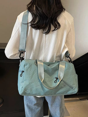 Light blue duffel bag with silver straps and multiple zippered pockets.