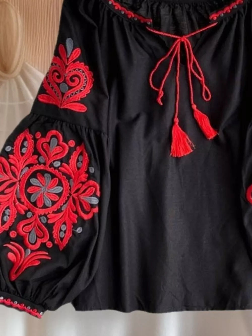 Black peasant blouse with red embroidery, tie neck, and tassel details.