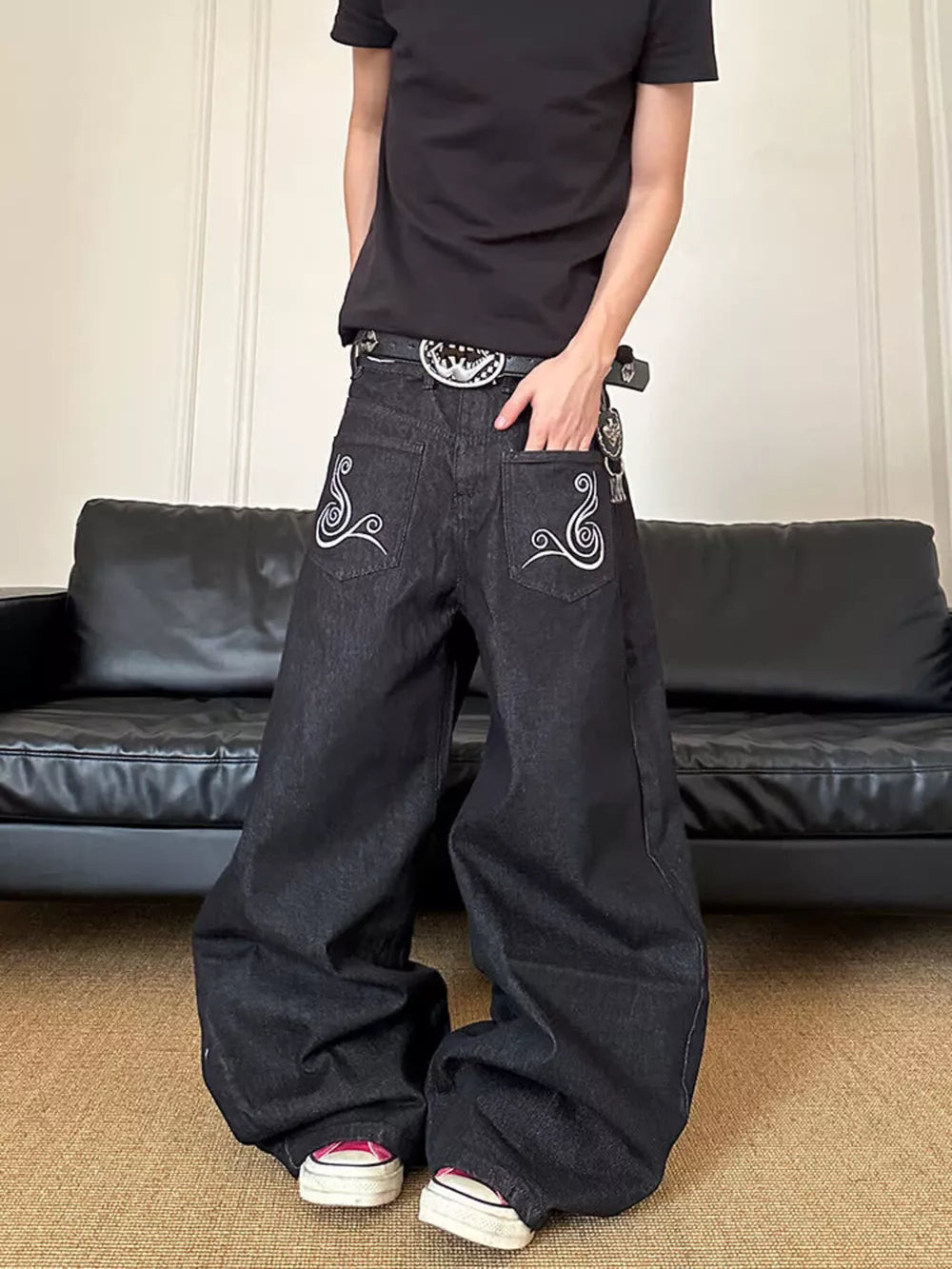 Men's dark wash wide-leg jeans with white embroidered back pockets and a silver buckle belt.