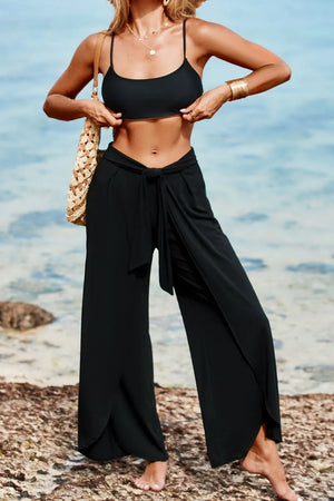 Black wrap-front palazzo pants with slit hem and tie waist, styled with a bikini top.