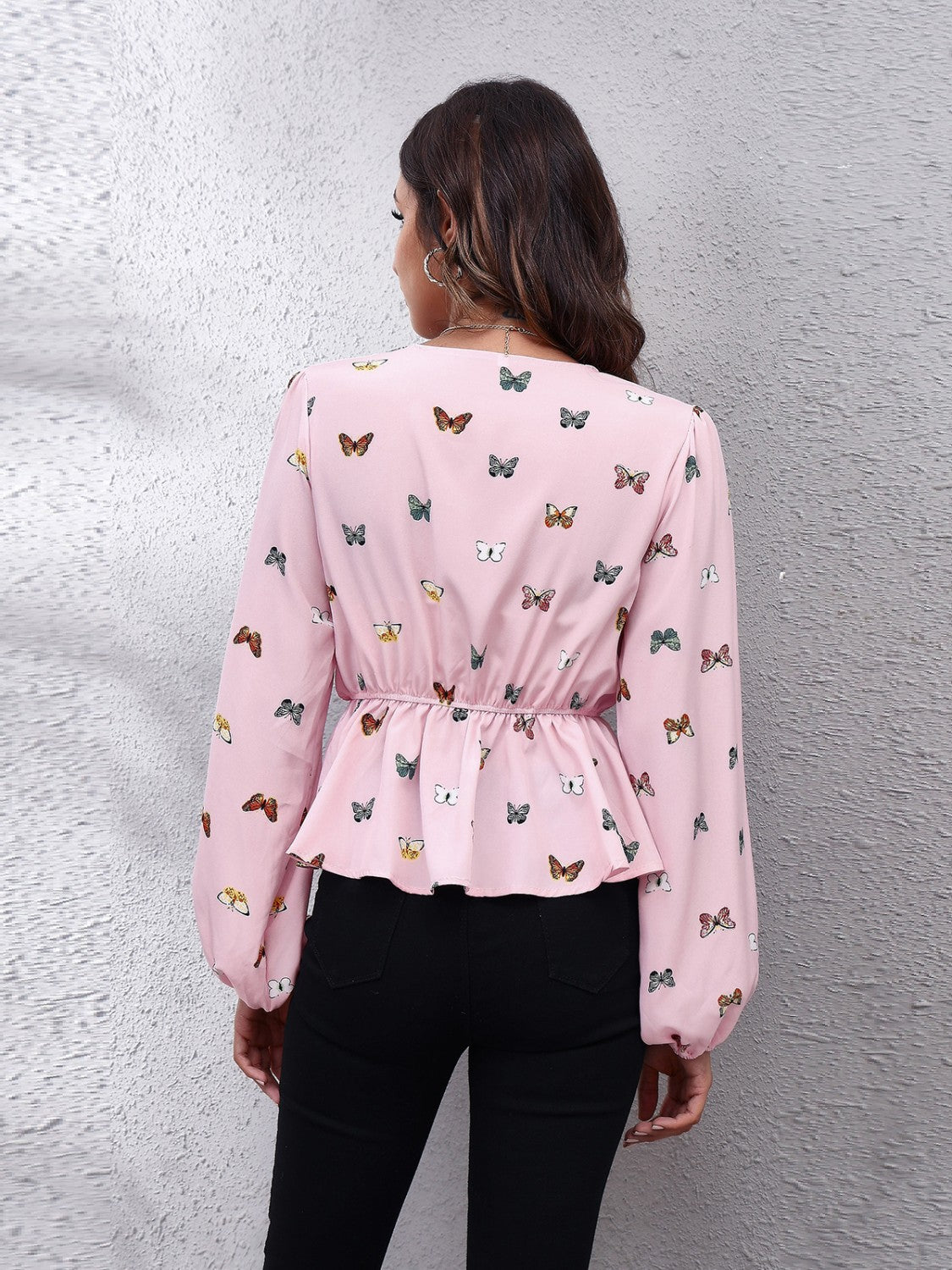 Blush pink peplum blouse with allover butterfly print, cinched waist, and balloon sleeves.