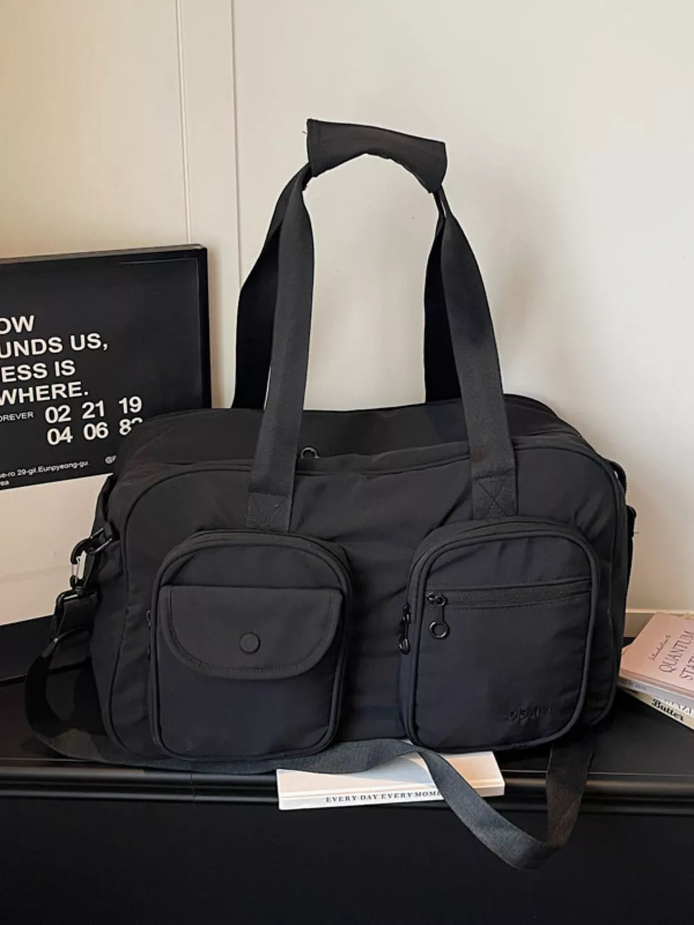 Black nylon duffle bag with multiple front pockets and adjustable strap.
