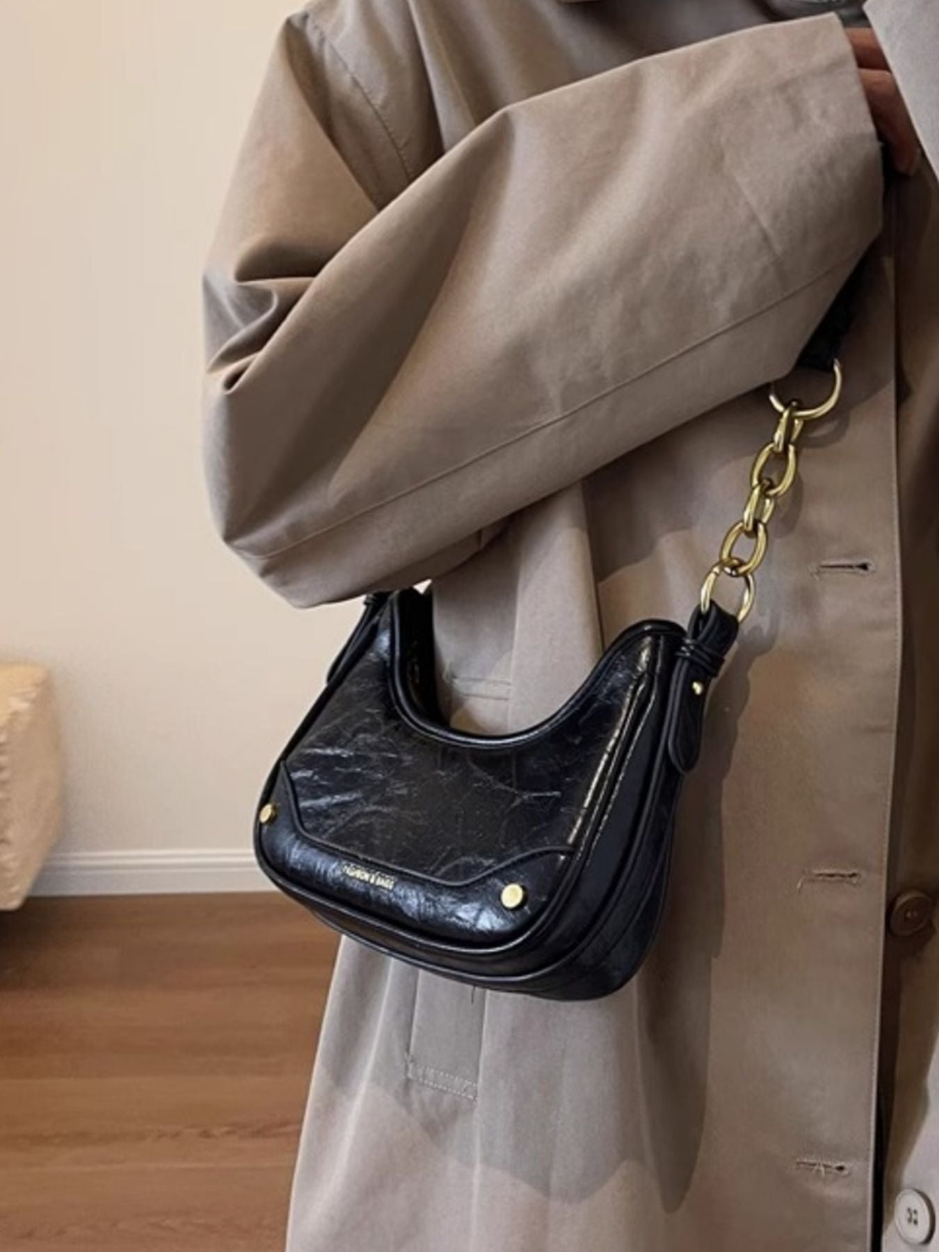 Black shoulder bag with chunky gold chain accent and crescent shape.