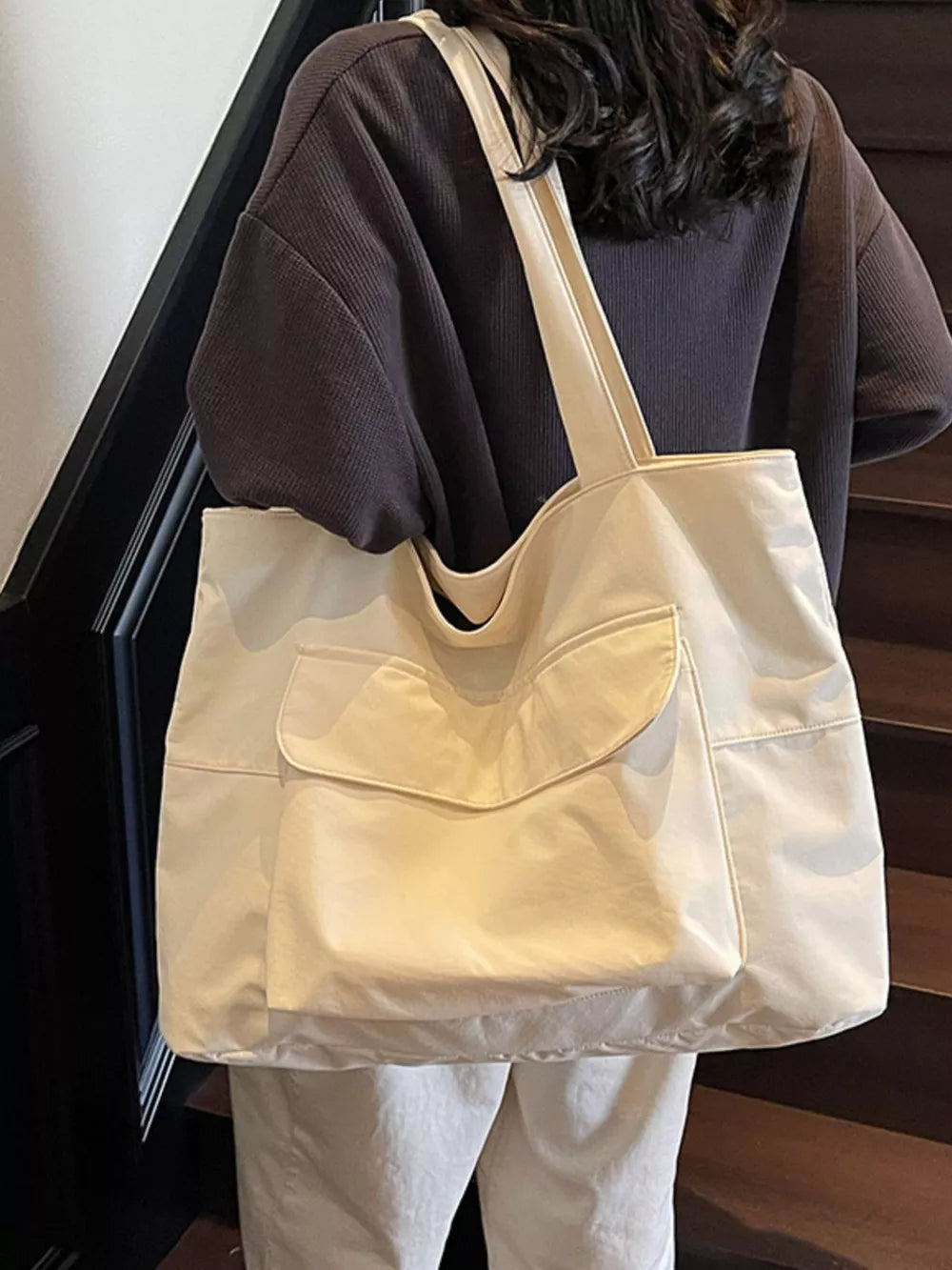Spacious cream nylon shoulder bag with flap and front pockets.