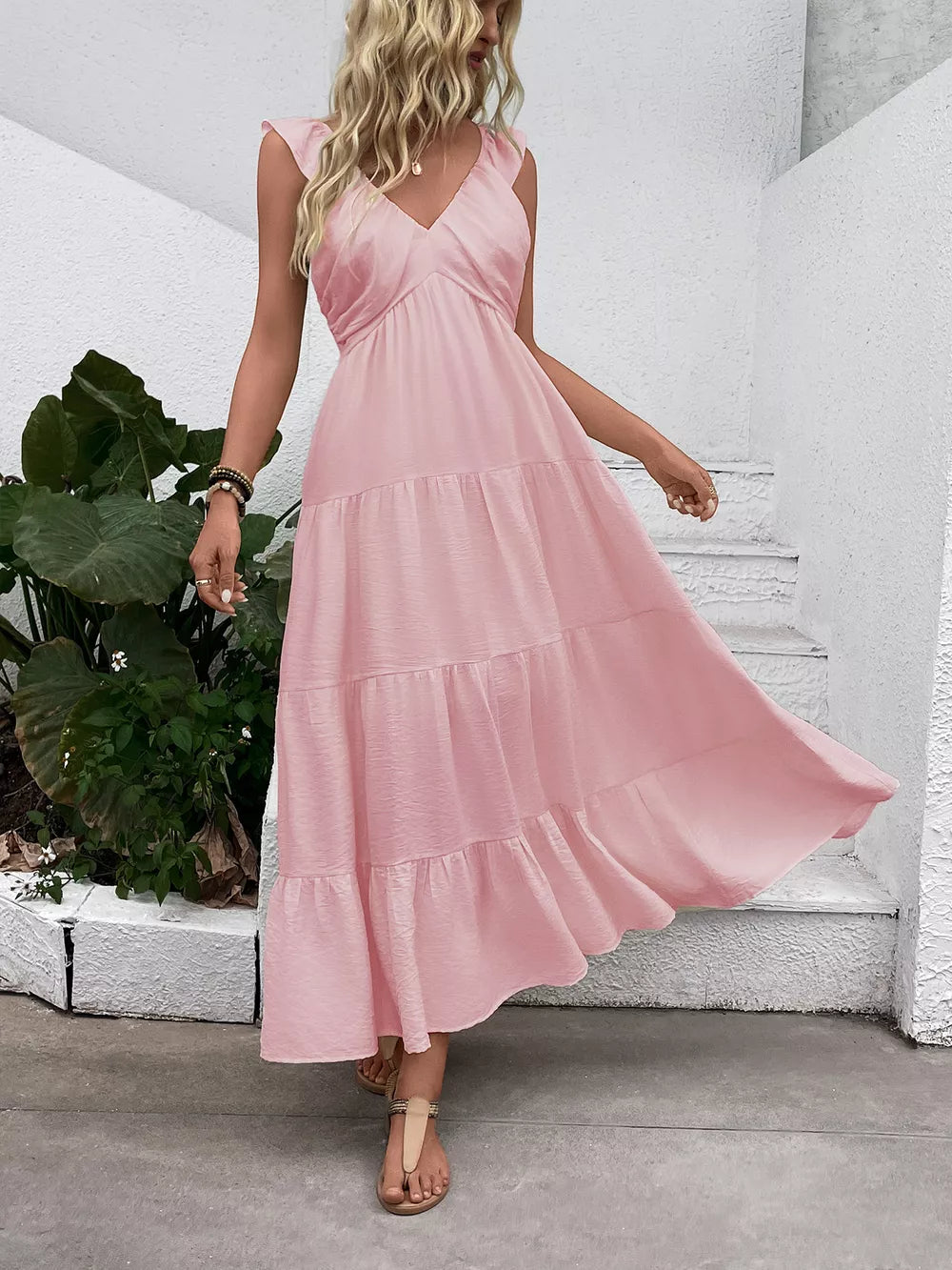 Blush pink tiered maxi dress with flutter sleeves and V-neck, flowing skirt.
