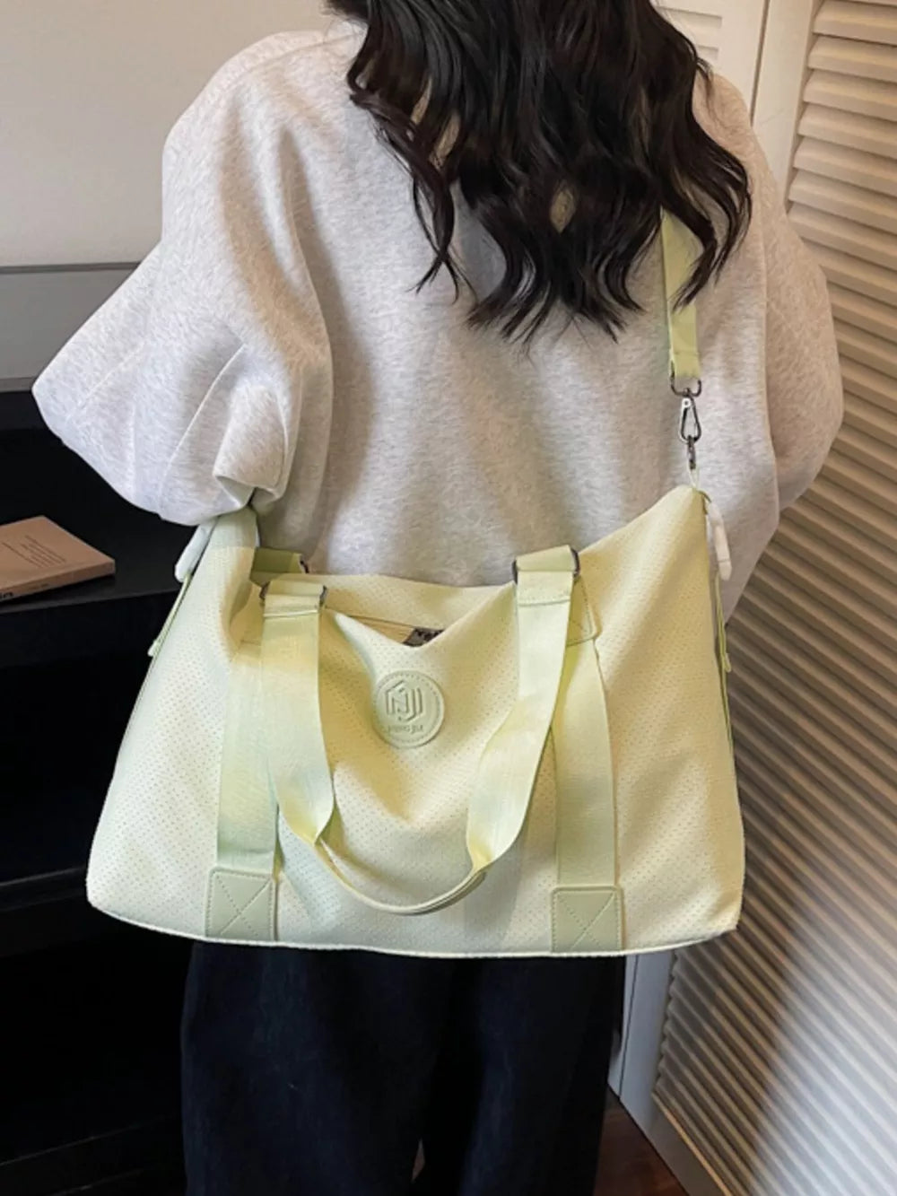 Chic perforated large duffle bag in pale green with dual handles and a crossbody strap.