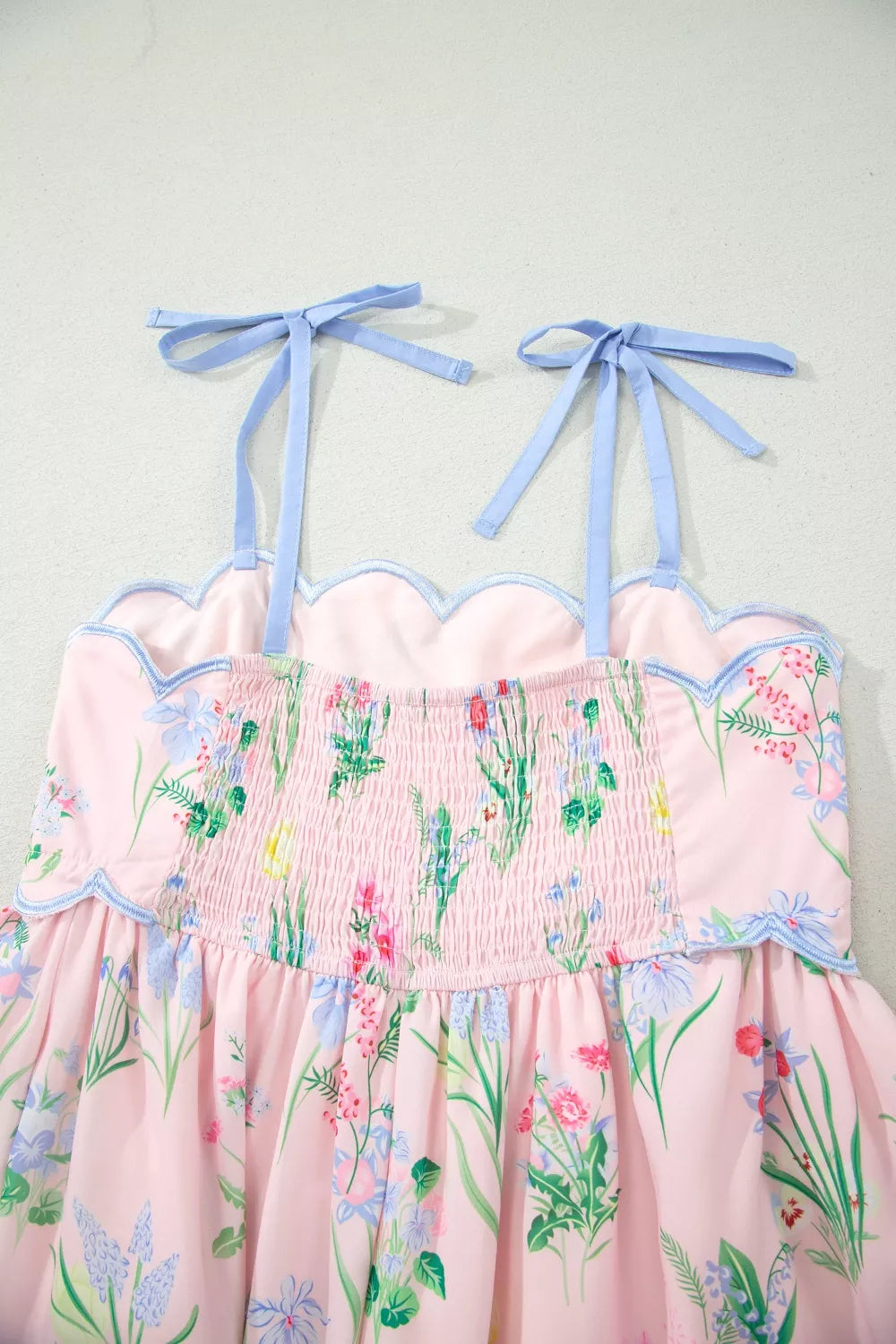 Pink midi dress with wildflower print, smocked bodice, scalloped trim, and blue tie straps.