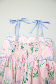 Pink midi dress with wildflower print, smocked bodice, scalloped trim, and blue tie straps.