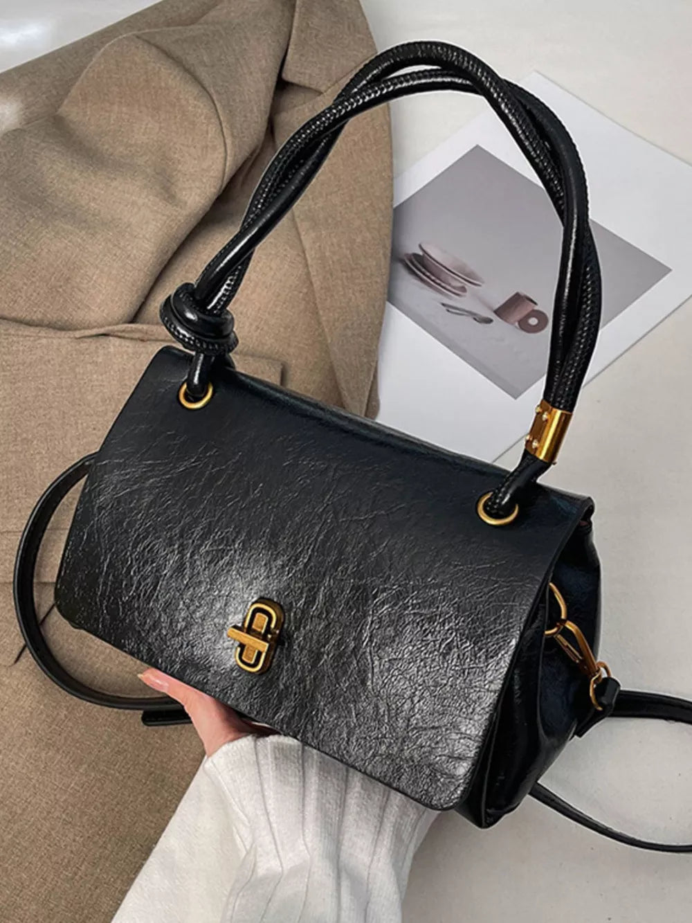 Black leather crossbody bag with twisted top handle and gold turn-lock closure.