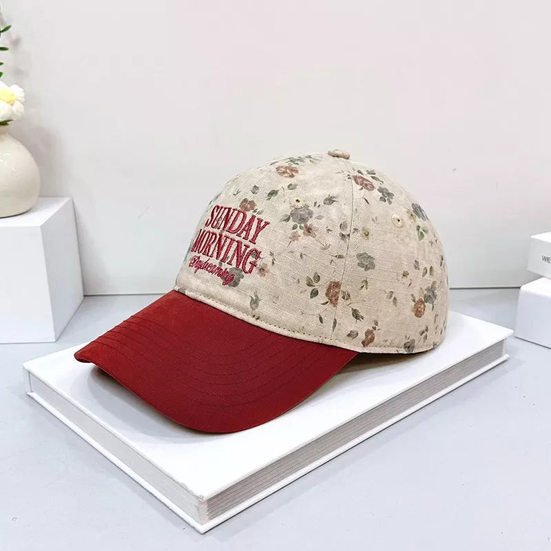 Cotton baseball cap with floral print and red brim, embroidered text.