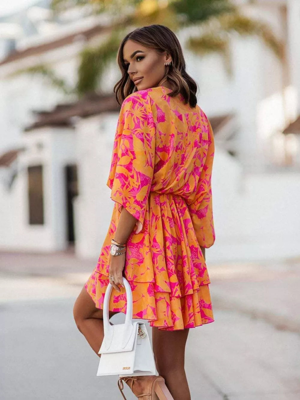 Tropical tiered mini dress in orange and fuchsia pink with a surplice neckline and belted waist.