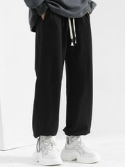 Men's black sweatpants with drawstring and loose fit, styled with white sneakers.