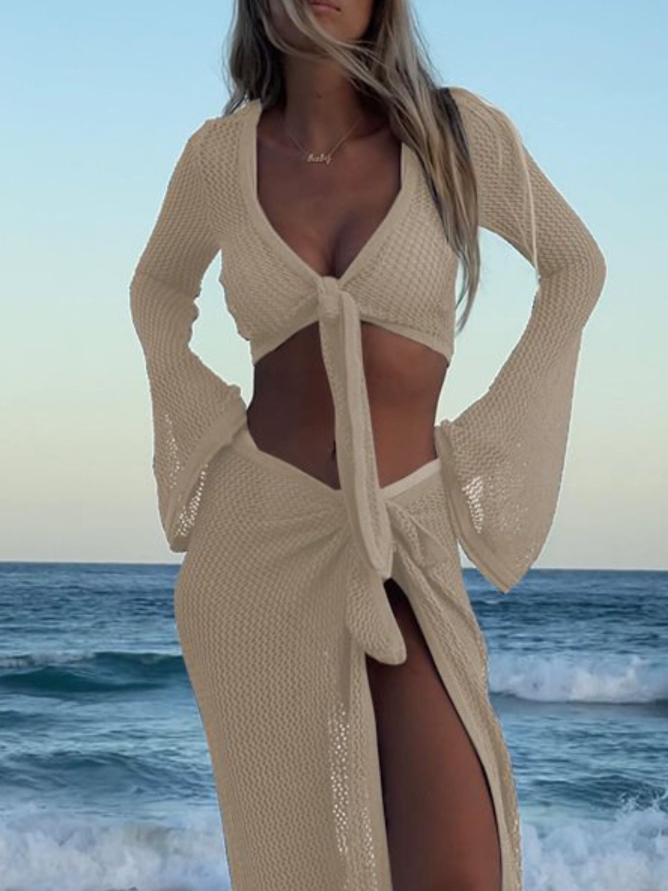 Beige openwork knit sweater set with tie front and bell sleeves, paired with a matching skirt with a high slit.