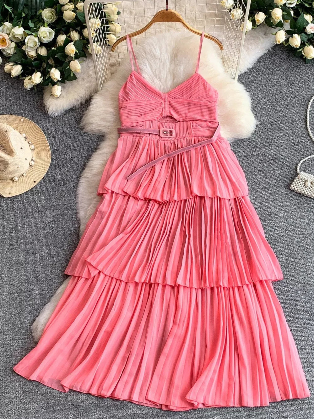 Pink pleated midi dress with spaghetti straps, V-neck, cut-out waist, and tiered skirt.