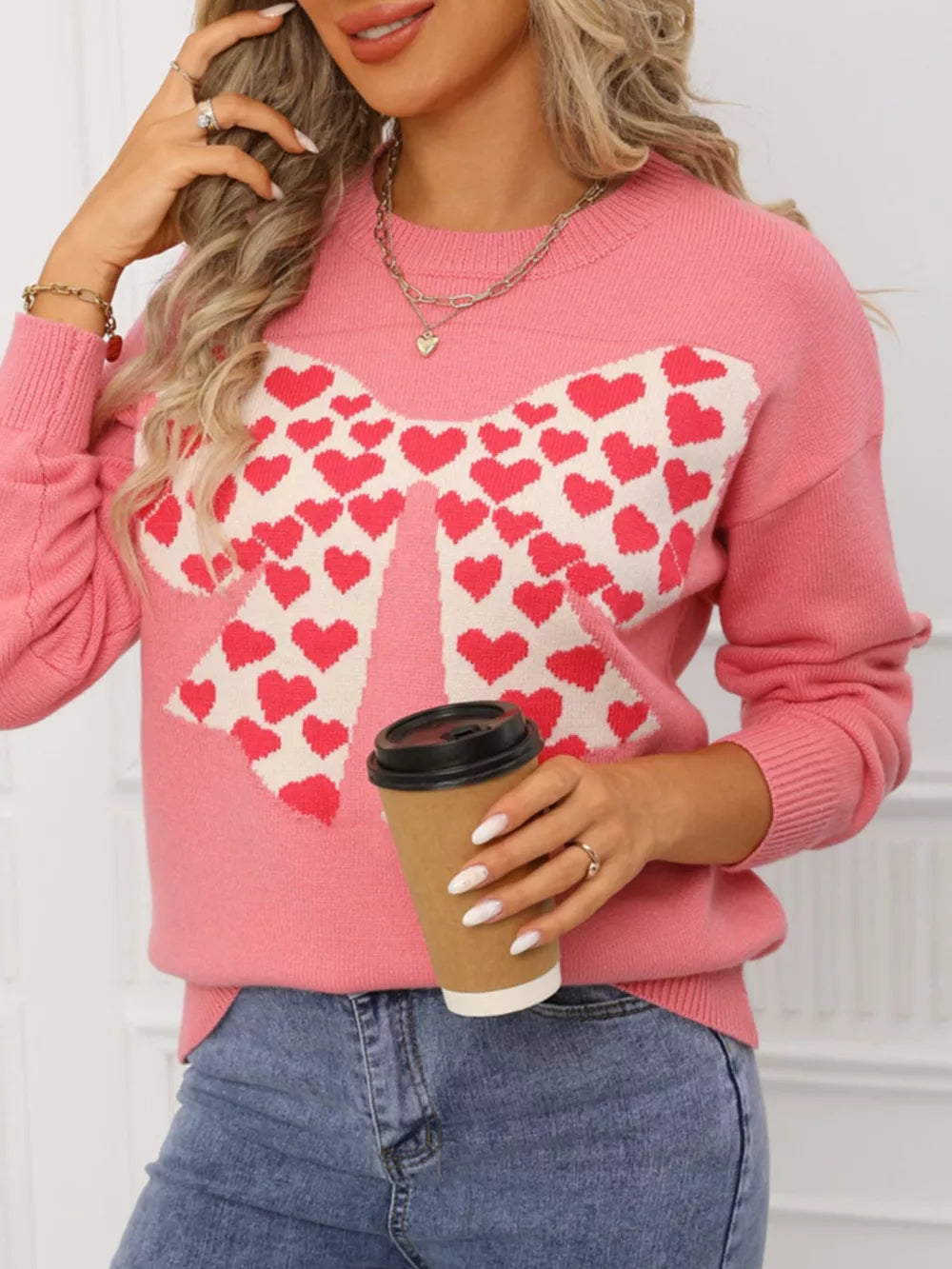 Pink acrylic knit sweater with a large white bow pattern filled with red hearts, round neck.