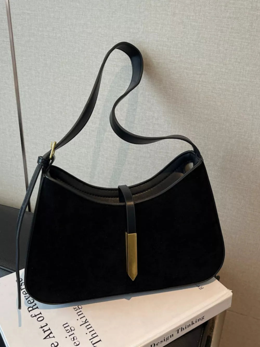 Black suede and leather curved shoulder bag with gold hardware detail.