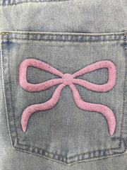Light wash denim jeans with a pink embroidered bow detail on the back pocket.