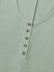Sage green waffle knit button-down romper with round neckline and brown buttons.
