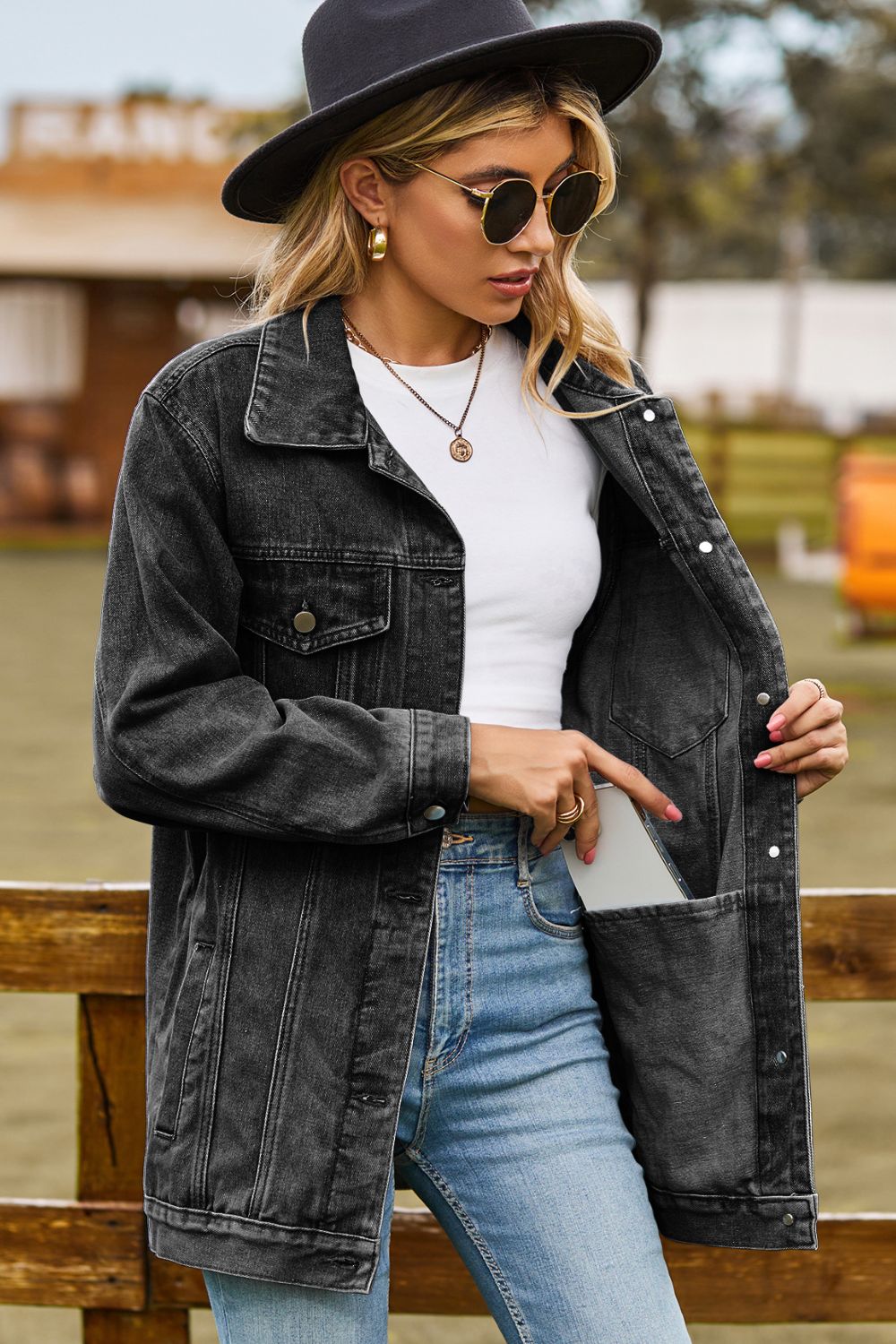 Black oversized denim trucker jacket with classic buttoned pockets and a phone in the side pocket.