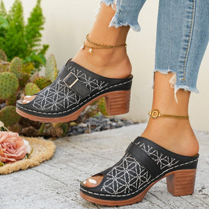 Black block heel sandals with white floral embroidery and buckle detail.