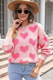 Blush pink knit sweater with textured heart motif, crewneck, and long sleeves.