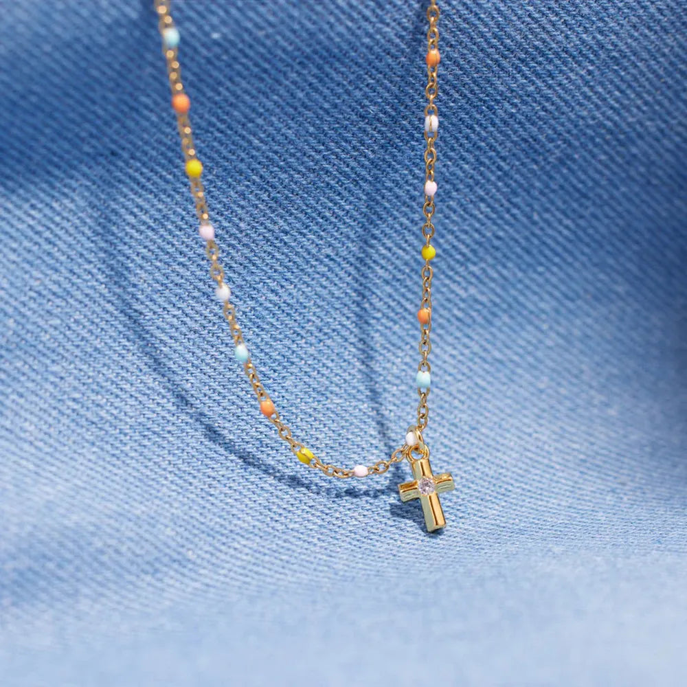 Gold necklace with rainbow beads and a small cross pendant with a clear stone.