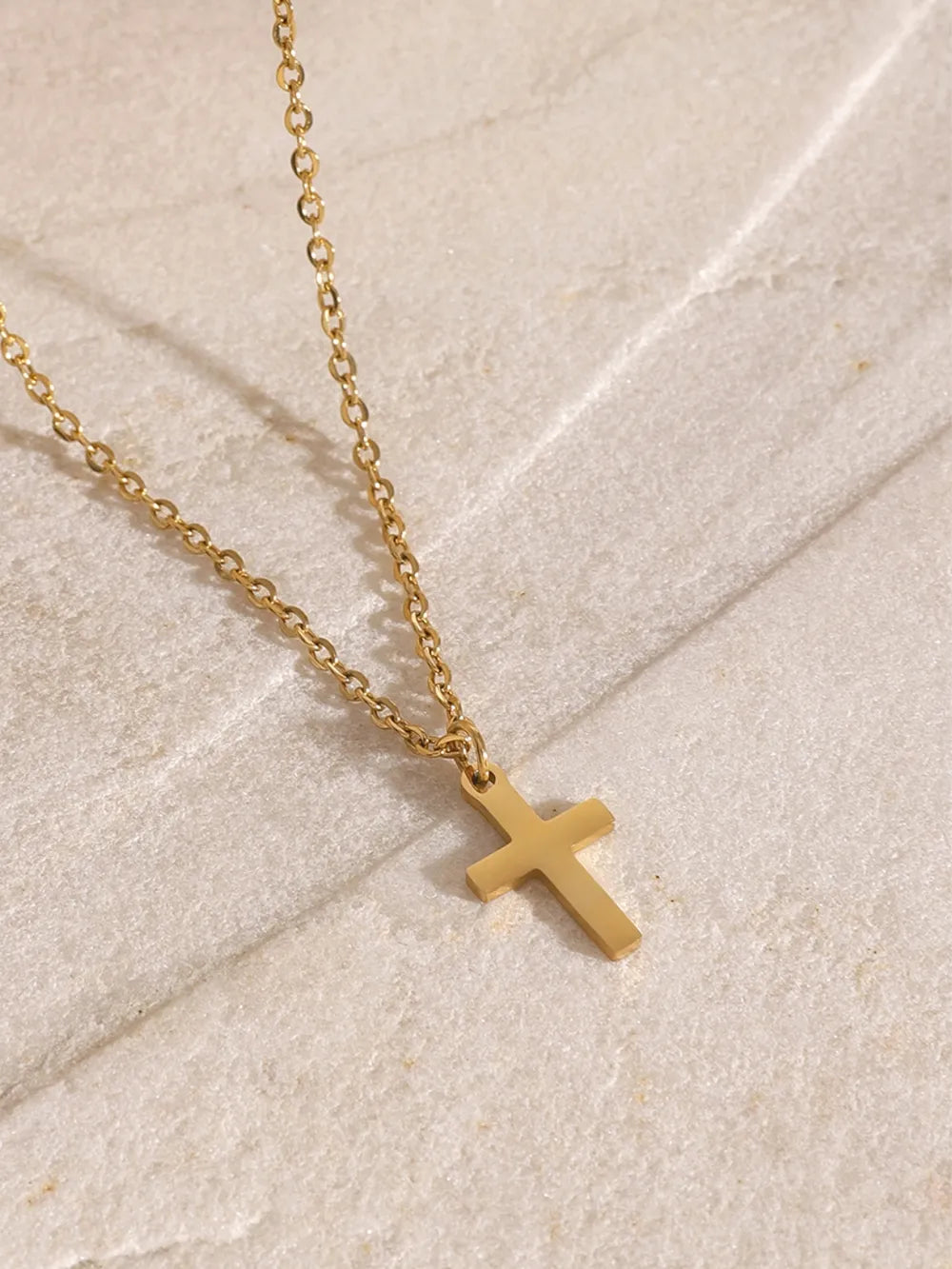 Gold layered necklace with a simple cross pendant on an adjustable chain.