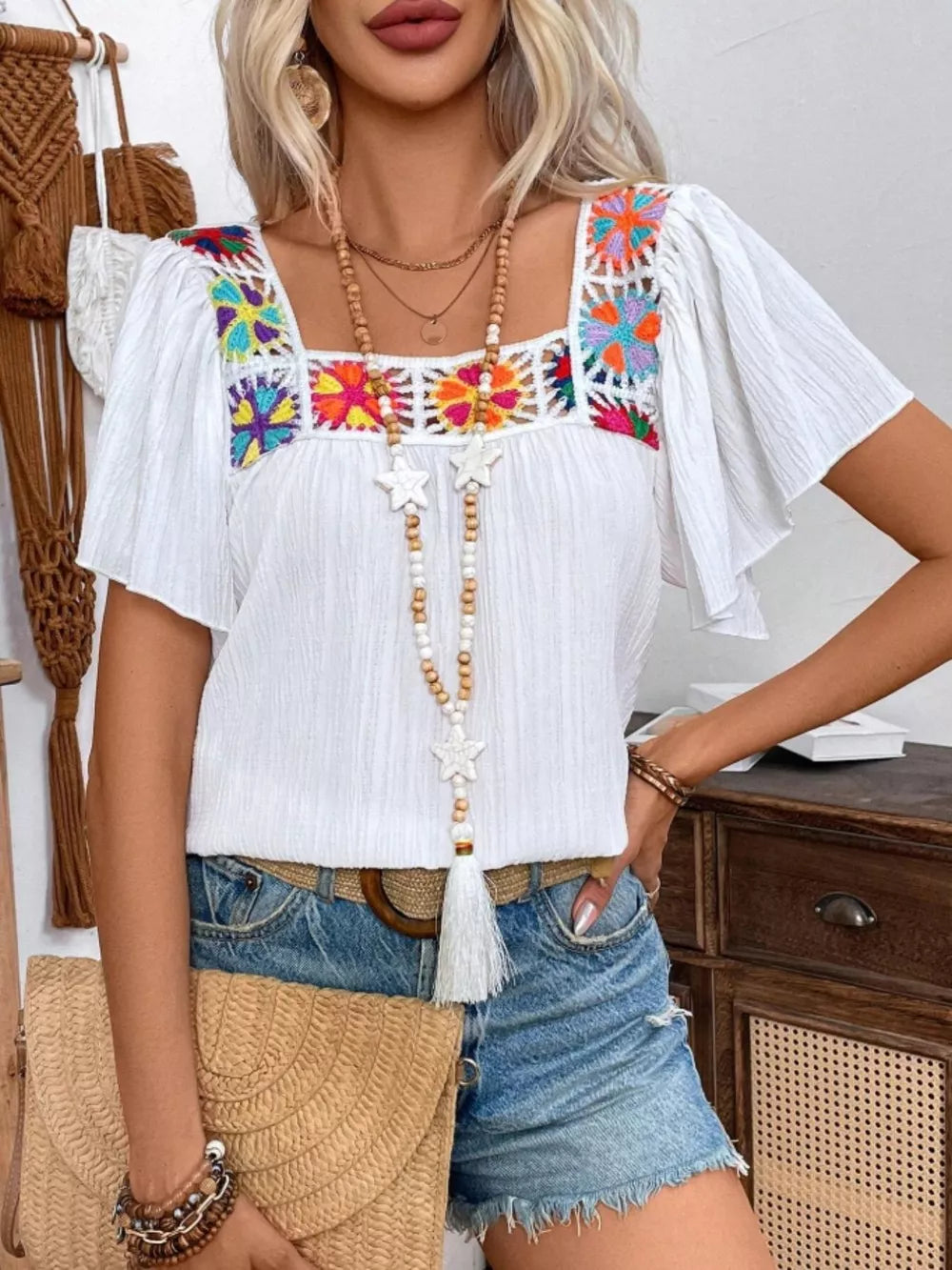 White embroidered square neck blouse with flutter sleeves and colorful floral details.