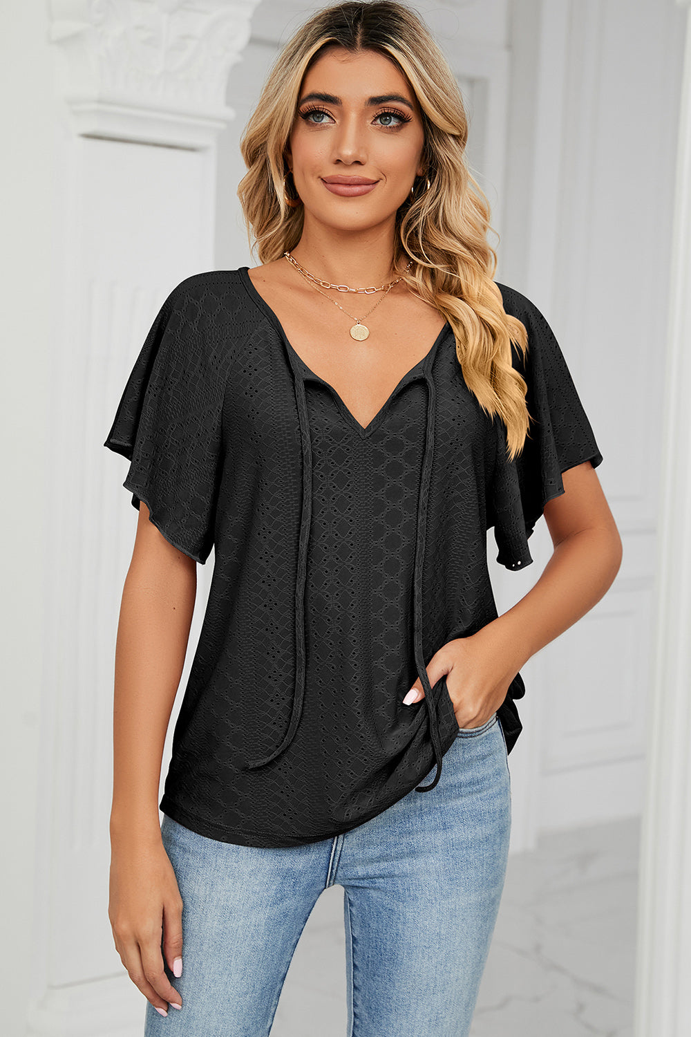 Black eyelet tie-neck blouse with flutter sleeves and V-neckline.