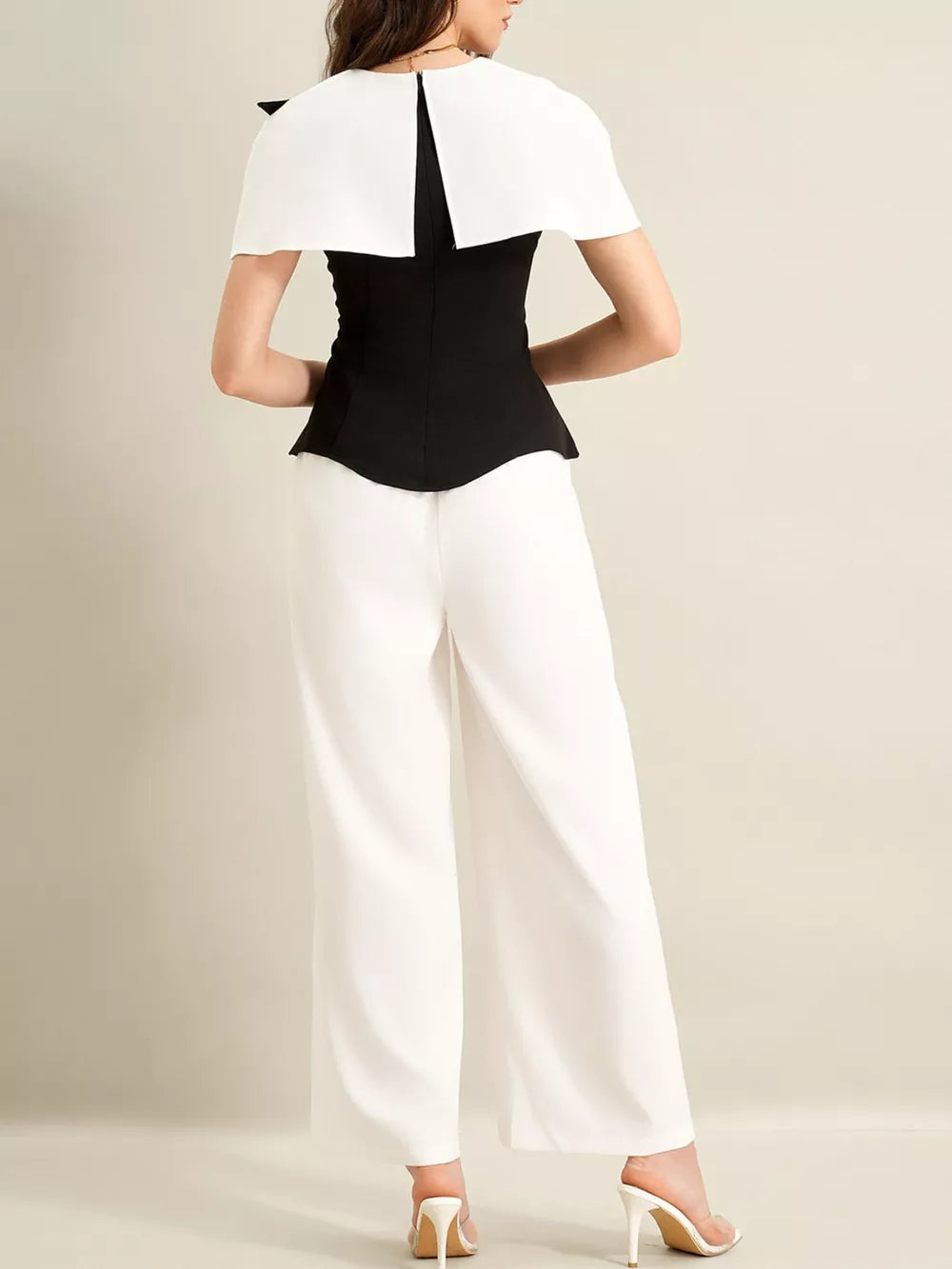 Black peplum top with white cape detail and white wide-leg pants.