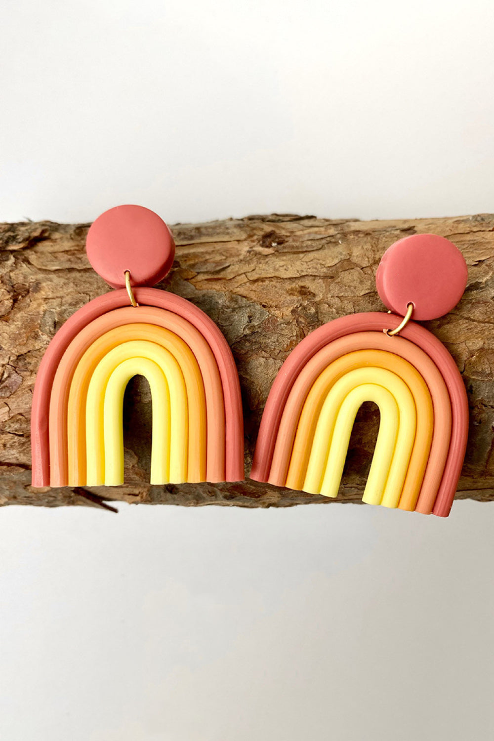 Rainbow arch clay earrings in coral, orange, and yellow with a round stud.