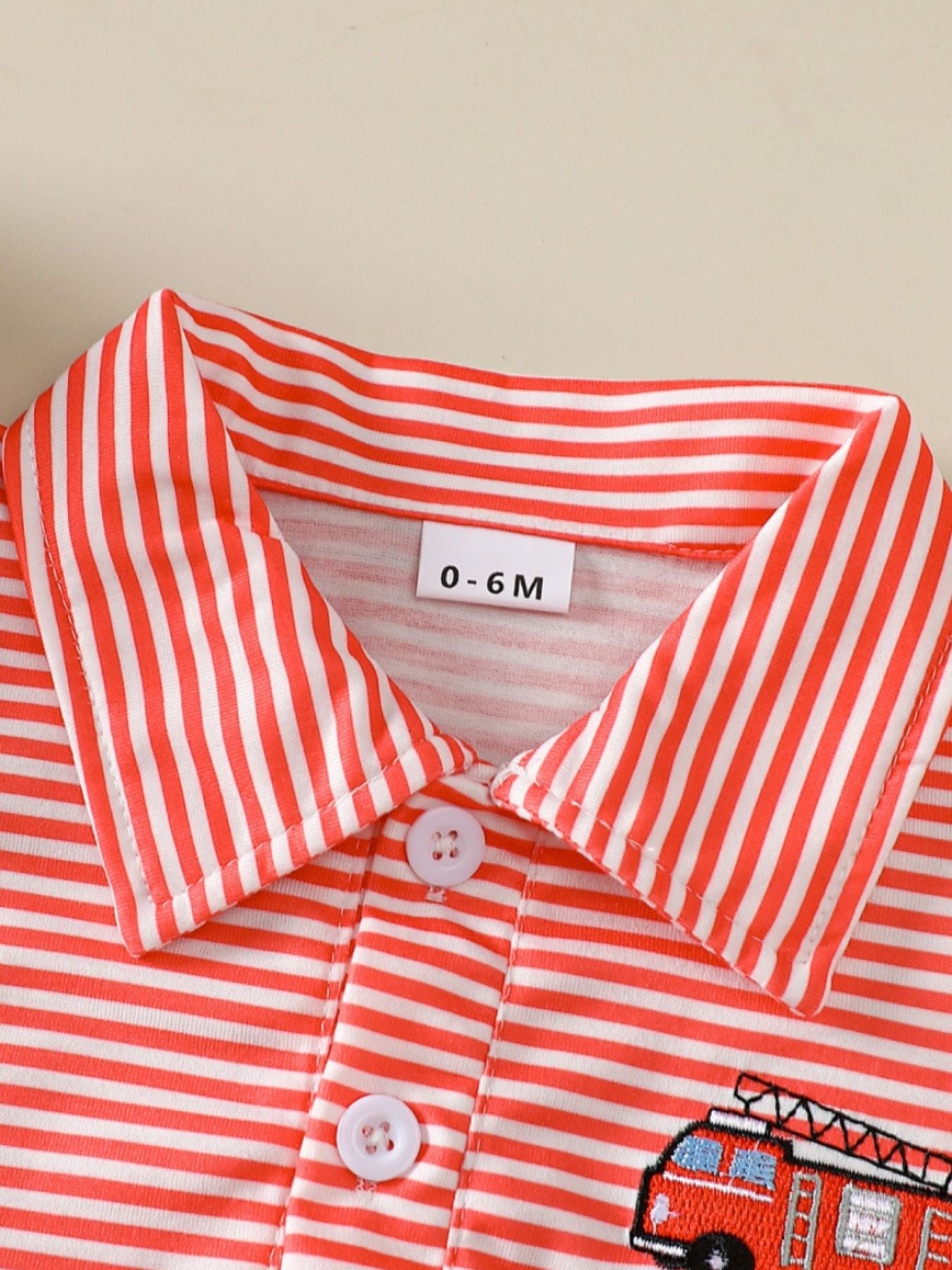 Coral striped baby polo shirt with embroidered firetruck detail and white buttons.