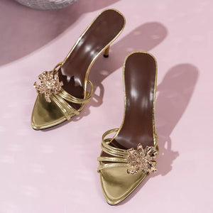 Gold high heel sandals with delicate straps and a floral embellishment.