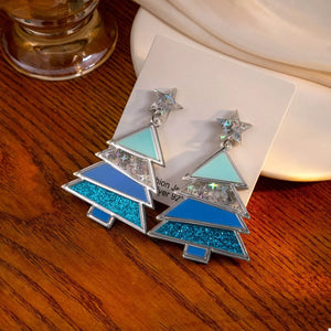 Whimsical Christmas tree dangle earrings in blue and teal acrylic with glitter and star details.