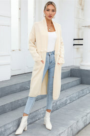 Ivory longline knit cardigan with fringe trim and pockets, styled with jeans and white boots.