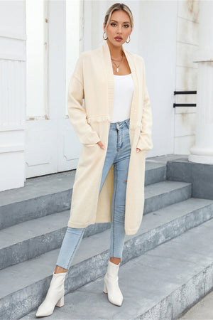Ivory longline knit cardigan with fringe trim and pockets, styled with jeans and white boots.